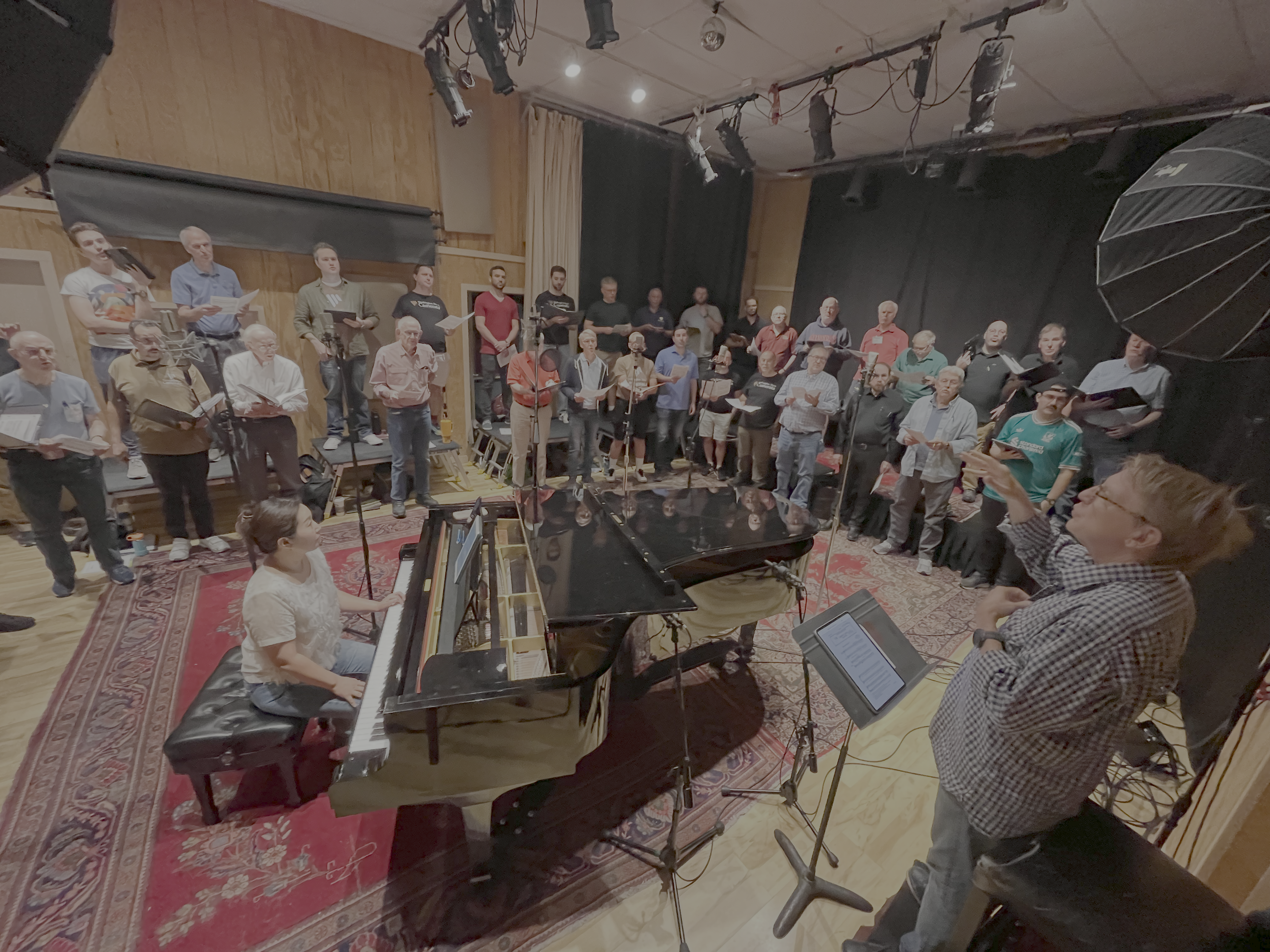 Washington Men's Camerata singing on a soundstage, with Scott Tucker directing and Grace Cho playing piano